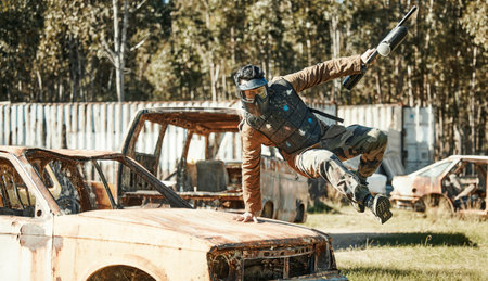 Paintball game, action and man jump car, agile and run in active battlefield, military playground or training arena. Army mission, gear and person in match competition, conflict or survival challengeの写真素材