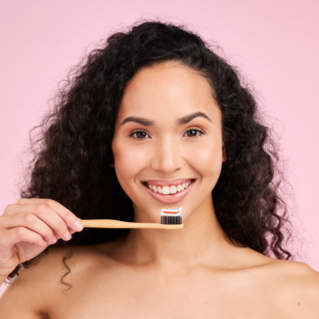 Woman, wood toothbrush and studio portrait for dental wellness, cosmetics and healthy mouth by pink background. Girl, model and natural toothpaste for teeth whitening, self care and dentistry productの写真素材