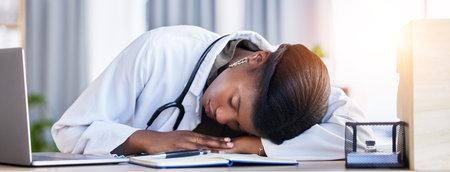 Tired doctor, woman and sleeping on desk in clinic office with stress, rest and dream in workplace. Overworked medic, fatigue and burnout in hospital, table and break for mental health in wellnessの写真素材