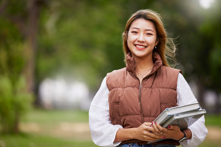 Asian student, portrait and woman with books for learning, education and outdoor on university campus with happiness or pride. Happy, face and girl in college with notebook or walking to classの写真素材