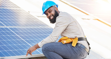 Black man, portrait and technician in solar panel installation on rooftop in city for renewable energy. Happy African male person, engineer or contractor working on roof in sun for electricity powerの写真素材