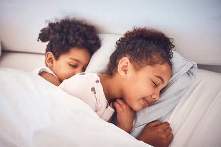 Girl, sleeping and children in bed in home with peace, comfort and rest with sisters, girls or friends together in bedroom. Kids, sleep and dream with happiness with pillow, blanket and duvetの写真素材