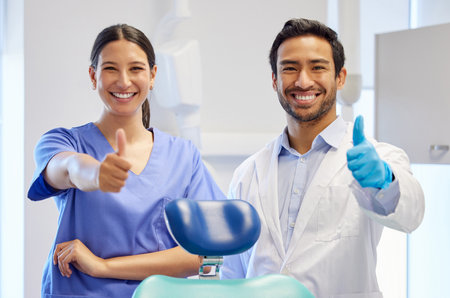 Dentist team, happy portrait and thumbs up for support, thank you or like emoji. Assistant woman and asian man or healthcare staff for dental care, oral health and wellness with a chair at practiceの写真素材