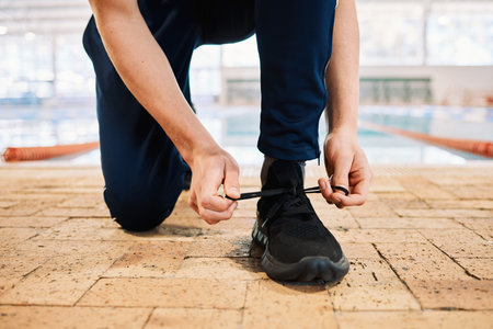 Man, hands and tying shoes by pool for workout, exercise or training preparation indoors. Closeup of...