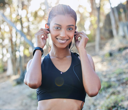 Sports, portrait and woman with a earphones for music, radio or podcast while running in nature. Fitness, exercise and female athlete doing cardio workout for race or marathon training in the woods.の写真素材