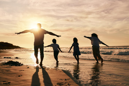Silhouette, family is running on beach and back view with ocean waves, sunset and bonding in nature. Energy, action people outdoor on tropical holiday and freedom, travel with trust and loveの写真素材