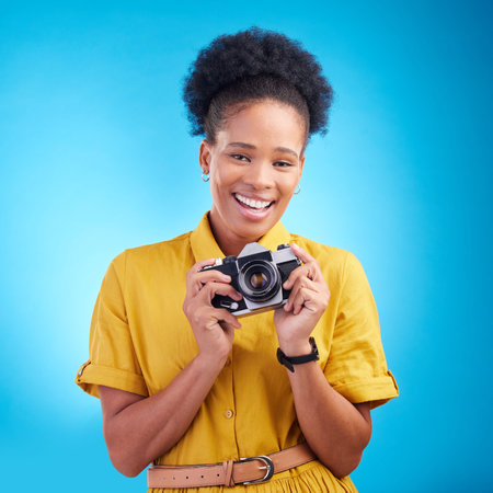 Photography, portrait and black woman with camera, smile and isolated on blue background, creative artist job and talent. Art, face of happy photographer with hobby or career in studio for photoshootの写真素材
