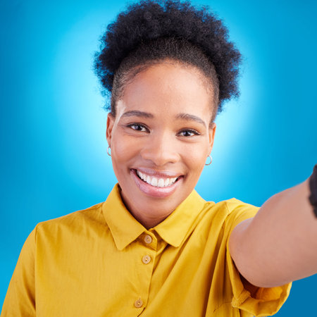 Happy woman, face and portrait smile for selfie, photography or memory against a blue studio background. African female person or photographer smiling for picture, photo or online social media postの写真素材