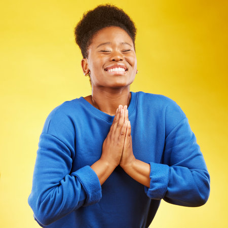 Thank you, hands and black woman praying in studio happy, relief and grateful on yellow background....
