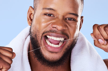 Portrait, man and floss teeth in studio, health dental and self care of gum gingivitis. Face of black male model, thread or cleaning mouth for fresh breath, tooth hygiene or plaque on blue backgroundの写真素材