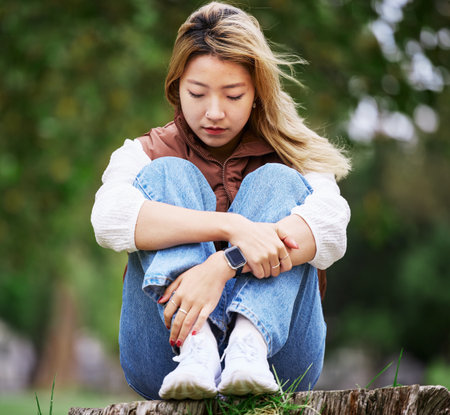 Student, sad and thinking with woman in park for depression, college and anxiety. Mental health, psychology and burnout with Asian person feeling lonely in nature for fatigue, pain and griefの写真素材