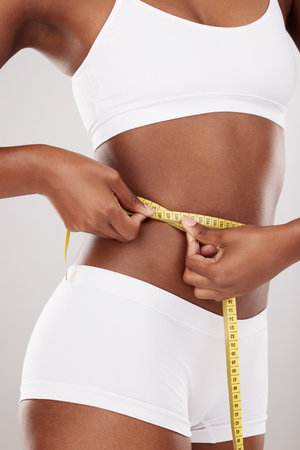 Tape measure, waist and stomach or body of woman for health and wellness on white background in studio. Fitness, progress and underwear of model on diet for weight loss goals, balance or motivationの写真素材