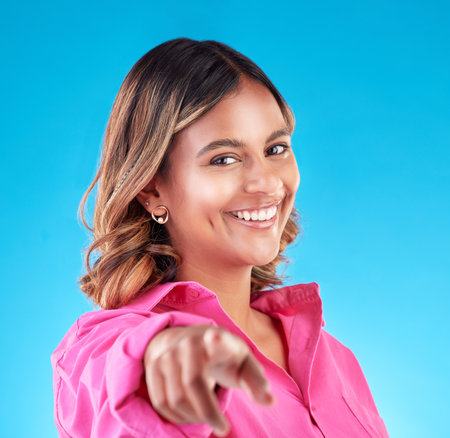 Pointing finger, smile and portrait of woman in studio to select, advertising or choice. Face of happy model person with hand or emoji for accountability, decision or choosing you on blue backgroundの写真素材