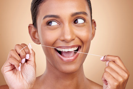 Woman, dental floss and studio for thinking, smile and cleaning for teeth whitening by brown background. Girl, model or happy for dentistry product, ideas or self care for cosmetic, beauty or healthの写真素材