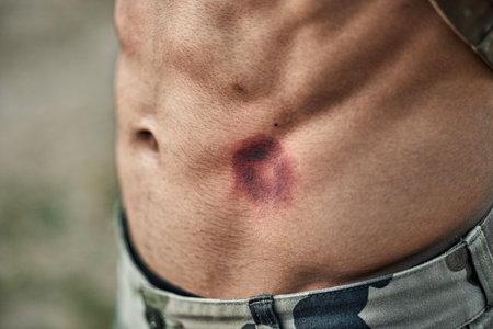 Paintball injury, stomach bruise and man in closeup with pain, shooting or accident for outdoor war games. Abdomen, emergency and wound in military training, zoom and battlefield for exercise in armyの写真素材