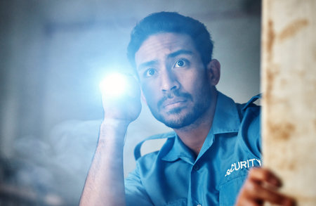 Flashlight, security guard and man in dark room for investigation, inspection and property search at...