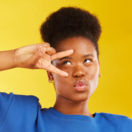 Peace, hand sign and a black woman in studio with pouting lips, confidence and a positive mindset. Emoji, icon and face of african female model person on yellow background with a v symbol and freedomの写真素材
