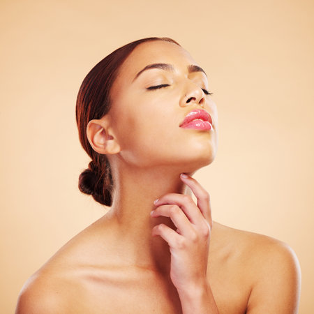 Face, relax or woman with natural beauty in studio isolated on brown background for wellness or glow. Facial treatment, hand or Brazilian girl model touch neck in self love, eyes closed or cosmeticsの写真素材