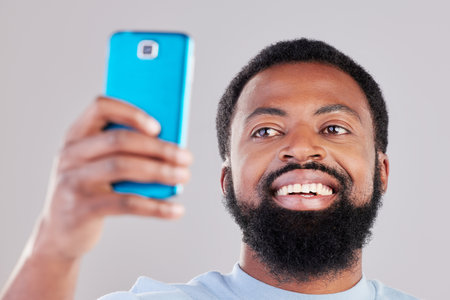 Happy black man, face and selfie in photography for social media, vlog or networking against a grey studio background. African male person smile for photo, memory or online communication and pictureの写真素材