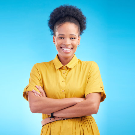 Black woman, portrait and happy in studio with a smile, confidence and a positive mindset. Fashion, arms crossed and African female model person in casual clothes on a blue background for motivationの写真素材