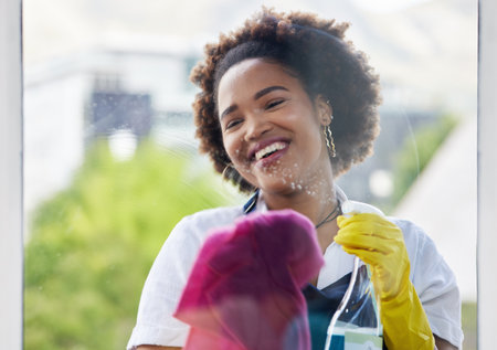 Black woman, cleaning spray and bottle on windows with cloth for hygiene of bacteria, dust and germs. Happy cleaner, housekeeping and chemical liquid for dirt, glass surface and hospitality servicesの写真素材