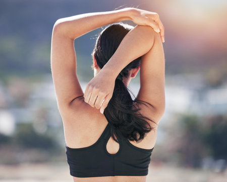Fitness, woman back and stretching arm in city for running, workout and body, exercise or wellness routine. Hands, stretch and behind lady runner outdoor for training, sports or physical performanceの写真素材