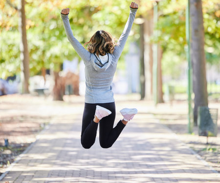 Fitness, jump and a woman outdoor for success at a park to celebrate win or achievement. Back of...