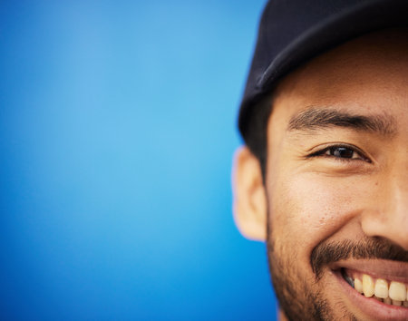 Studio, portrait and closeup on half of man in sports on blue background with advertising, mockup or space with athlete. Happy, face and smile with cricket or baseball cap and fitness or wellnessの写真素材