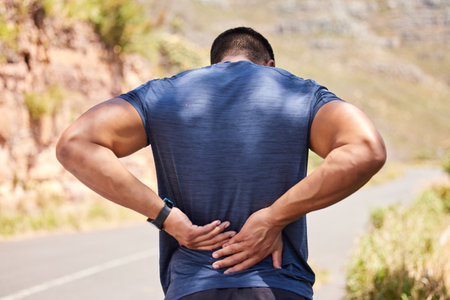 Sports man, runner and back pain from fitness training injury or running workout accident outdoors. Active person, hurt spine muscle or injured male athlete with exercise emergency on roadの写真素材