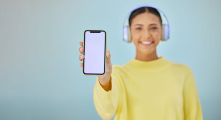 Happy woman with phone screen, headphones and mockup in studio for social media post, mobile app and...