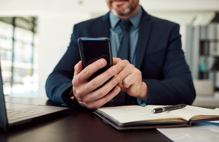 Hands, phone and notebook with a business man checking his calendar while planning in an office. Mobile, communication or test message with an employee reading a schedule at his desk in the workplaceの写真素材