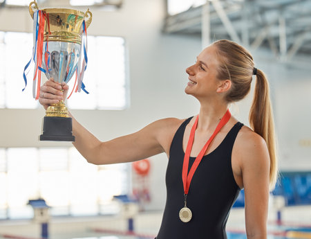 Swimming, trophy and winner in celebration with medal, achievement or happiness from success in the race or pool. Winning, competition and woman swimmer or athlete on sports podium with gold awardの写真素材