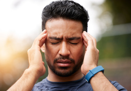 Face of sports man, headache and pain outdoor for injury, vertigo and tired of exercise problem. Sad asian athlete, sick runner and training with migraine, fatigue or stress of burnout for fitnessの写真素材