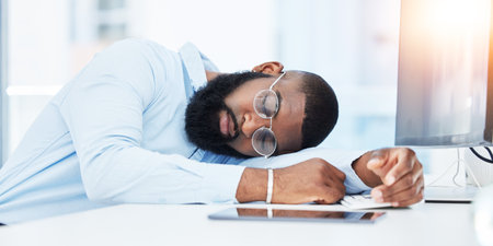 Sleeping, burnout and tired businessman in office overwhelmed by deadlines with fatigue at desk. Lazy worker, depressed consultant or exhausted black man resting or taking nap in overtime with stressの写真素材