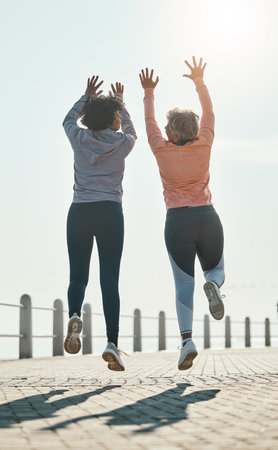 Fitness, jump and success with friends at beach for celebration, motivation and training. Cardio, workout and health with mature women in nature for running, energy and exercise goals togetherの写真素材