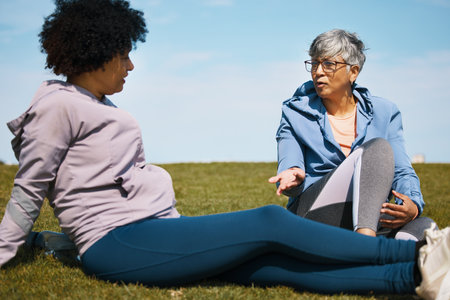 Talking, fitness and senior women friends on the grass outdoor taking a break from their workout routine. Exercise, training and summer with elderly people in conversation on a field for wellnessの写真素材
