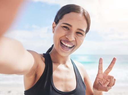 Fitness, selfie and woman at beach with peace hands for running, sports or exercise in nature. Portrait, happy and lady health and wellness influencer smile for social media, blog or profile pictureの写真素材