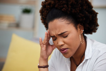 Woman, headache and stress in debt, financial crisis or burnout on sofa at home. Face of African female person with bad head pain, migraine or mental health strain from pressure or difficultyの写真素材