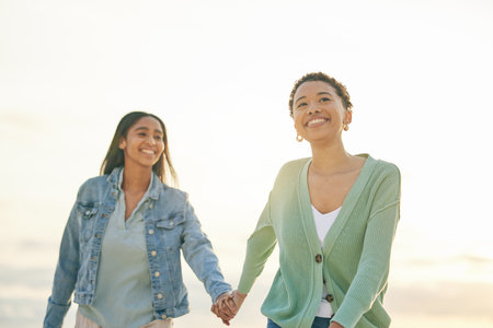 Love, beach and smile, lesbian couple holding hands and walking together on sunset holiday adventure. Lgbt women, bonding and relax on ocean vacation with romantic date, pride and happy nature travelの写真素材