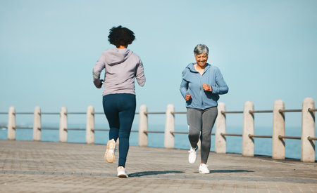 Running, fitness and senior friends by sea with mature women and smile from marathon. Exercise, workout and training on beach promenade path for health and wellness in the morning with happy peopleの写真素材