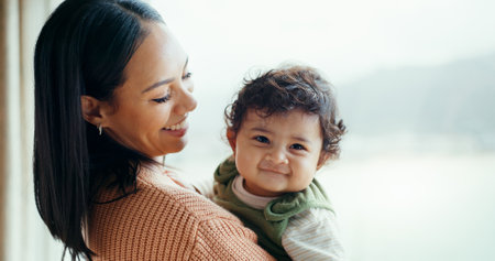 Mother, newborn and smile by window, home and happy together with care, love and bonding in childhood. Mom, infant baby and excited with connection, development and hug at family house in Canadaの写真素材
