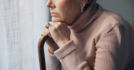 Thinking, window and hands of old woman and walking stick in bedroom for wellness, retirement and healthcare. Depression, mental health and nursing home with closeup of patient with a disabilityの写真素材