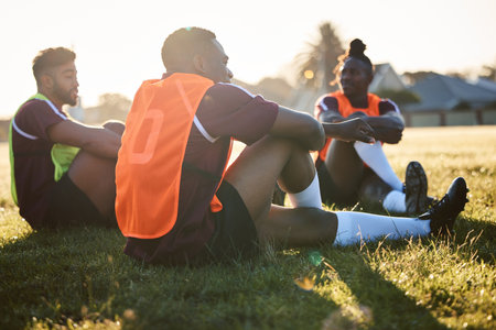 Rugby, team and men relax on field outdoor, talking and communication at sunrise in the morning. Sports, athlete group and players sitting on grass after exercise, training or friends workout in gameの写真素材