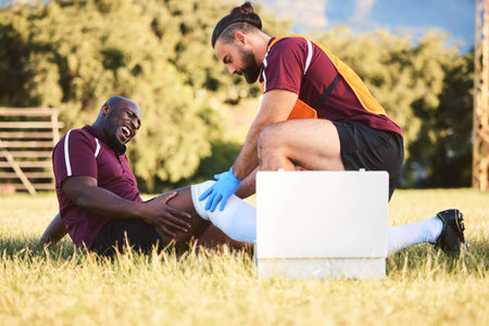 Black man, knee pain and injury, medic help athlete and sports accident on field with health and wellness. Bandage leg, male healthcare worker and support with medical care, inflammation and fractureの写真素材