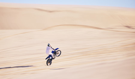 Bike, sand and fitness with a man in the desert for adrenaline, adventure or training in nature. Motorcycle, speed and balance with an athlete riding a sports vehicle on space in summer for freedomの写真素材