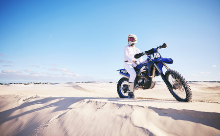 Sand, motor sports and man with motorbike for adrenaline, adventure and freedom in desert. Action, extreme challenge and male person on bike on dunes for training, exercise and race or competitionの写真素材