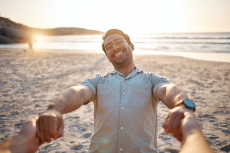 Happy, portrait and a couple holding hands at the beach for swinging, care and love on vacation. Sunset, travel and an Asian man with a person for freedom, summer fun or support on holiday at the seaの写真素材