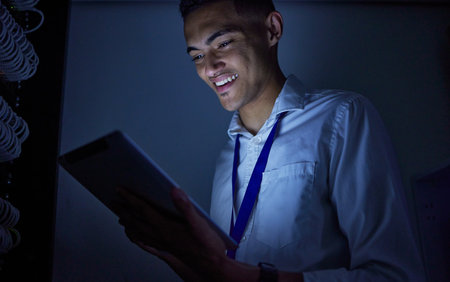 Man, tablet engineering and server room or data center management, system solution or cybersecurity at night. Happy, electrician person on digital tech with power, electricity or programming in darkの写真素材