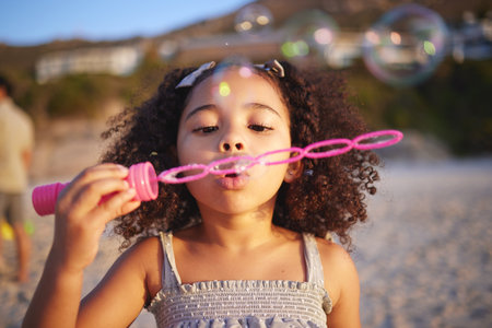 Girl child, beach and blowing bubbles with playing, outdoor and freedom on sand, games and thinking in nature. Female kid, soap and water with plastic toys with wind, summer sunshine and vacationの写真素材