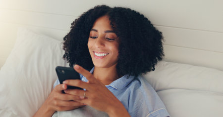 Phone, happy woman and bed of a young female texting on a social media app in the morning. Wifi, web networking and happiness of a young person with a smile in a house writing a text in a chatの写真素材